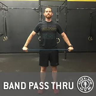 A man with a beard stands in a gym setting, wearing a black t-shirt with text and holding a barbell in front of a sign that says "BAND PASS THRU".