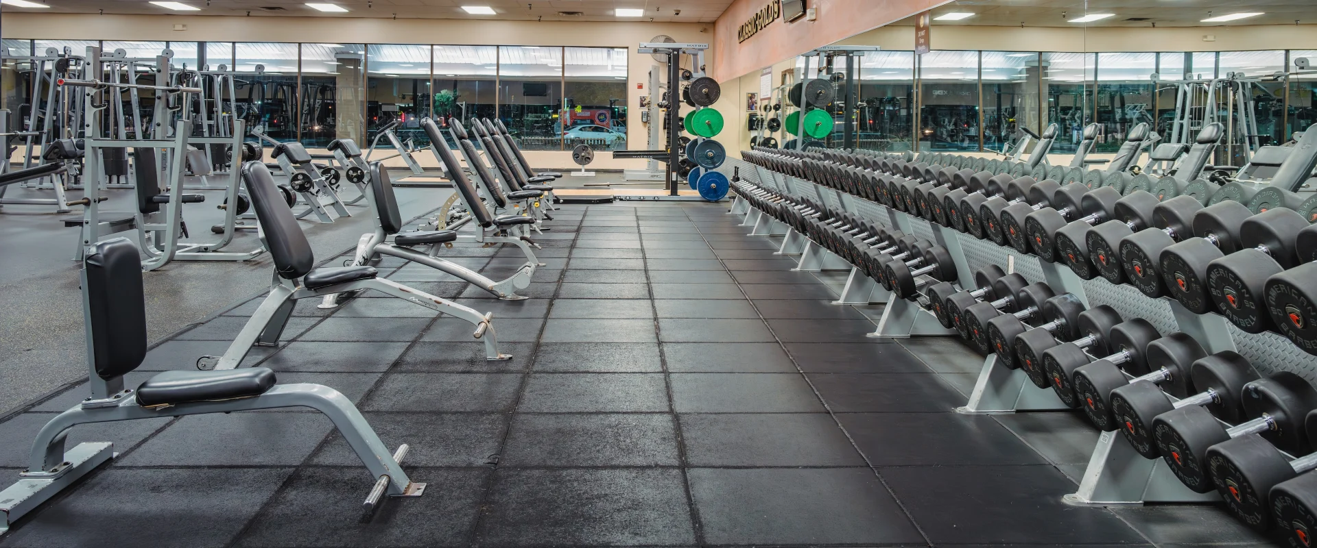 Dumbbell area at Gold’s Gym in Austin (Southeast), showcasing a long rack of neatly organized dumbbells in front of mirrored walls. Adjustable benches are positioned nearby for free weight exercises, with additional strength equipment visible in the background.