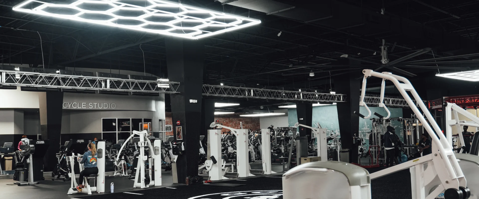 A wide view of training equipment positioned near the cycle studio at Gold’s Gym Randleman, with geometric LED lighting overhead, strength equipment arranged throughout the floor, and open space leading toward additional training zones.