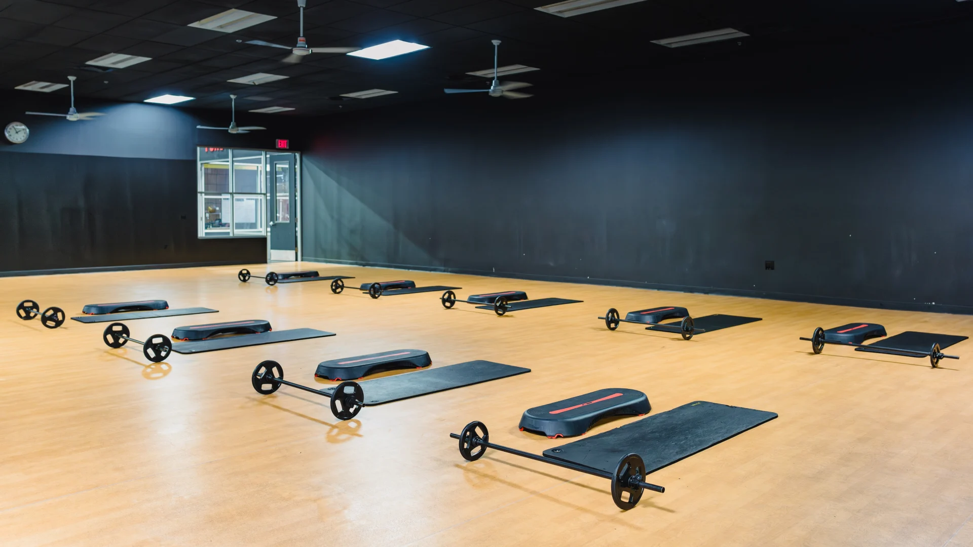 Empty fitness studio with step platforms, mats, and barbells arranged for a group workout.