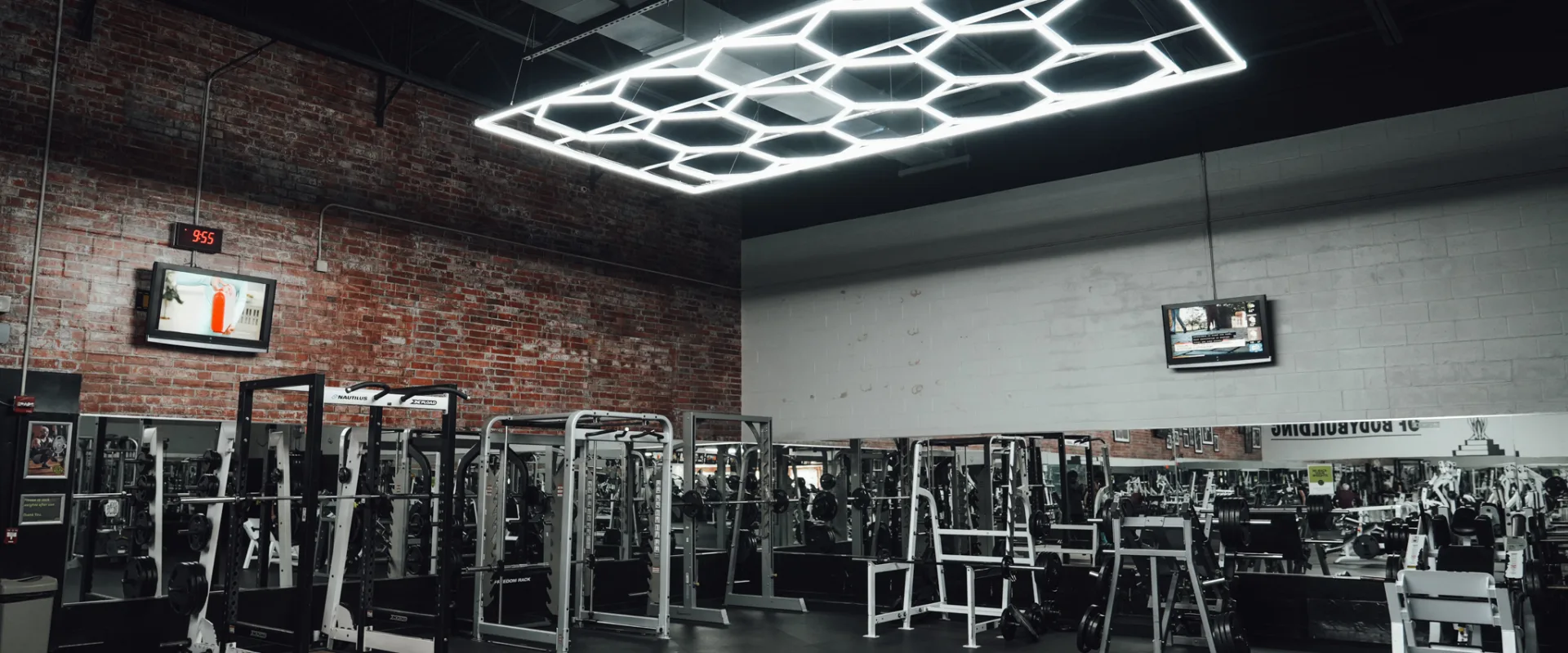 A free weights section at Gold’s Gym Randleman with squat racks, benches and mirrored walls. A brick accent wall and LED lighting contribute to the industrial-style interior.