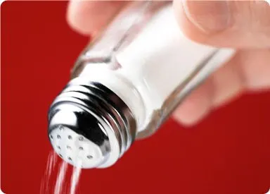 A close-up view of a salt shaker pouring salt onto a red surface.