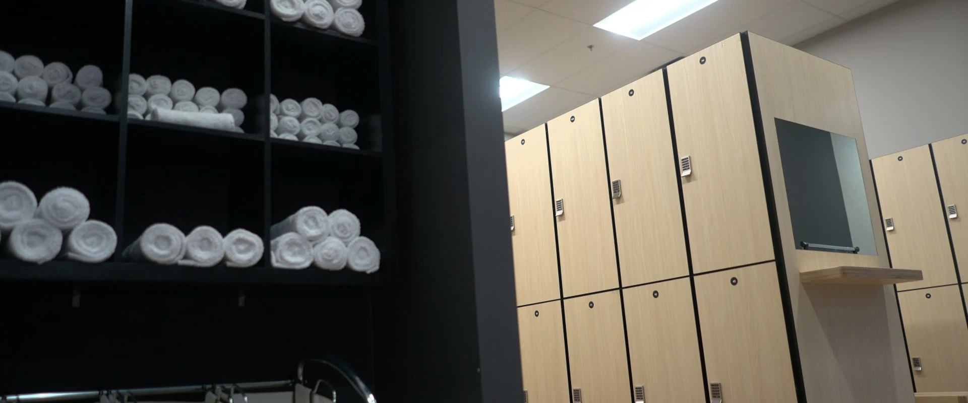 VIP private locker room at Gold’s Gym Laval with cubby shelves stacked with white towels, laundry hampers, and natural wood lockers paired with a vanity and mirror station.