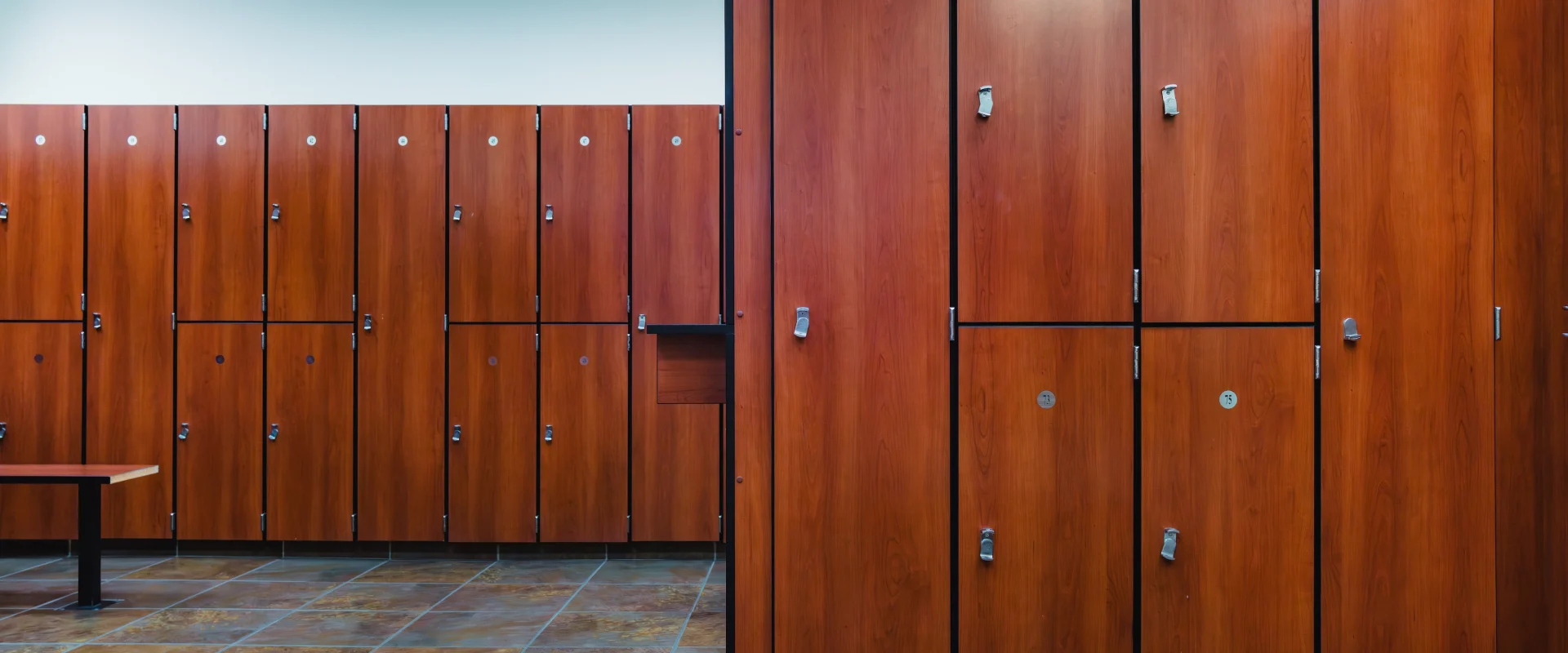 Locker room at Gold's Gym Fiesta Trails with wooden lockers and a tiled floor. Benches are positioned in front of the lockers, creating a tidy and orderly atmosphere.