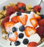 A plate filled with a colorful assortment of fresh fruits, including strawberries, blueberries, and sliced oranges, alongside a serving of granola or cereal.