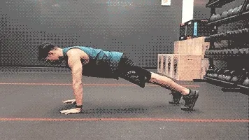 A person in athletic attire is performing a push-up exercise on a gym floor, with various fitness equipment visible in the background.