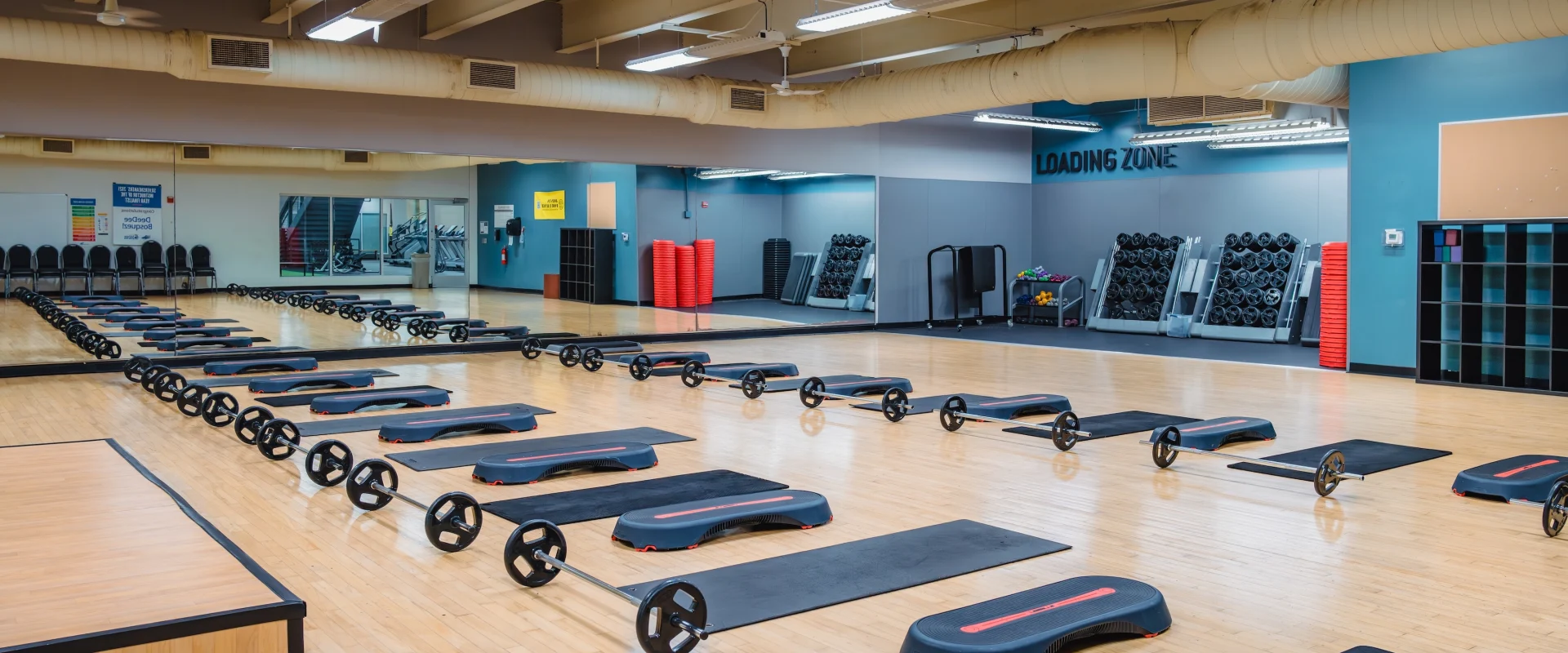Group exercise room set up with multiple mats, steppers and weight bars.