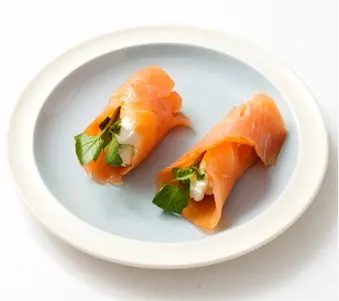 The image shows two slices of smoked salmon wrapped around a filling of what appears to be cream cheese and fresh herbs, served on a white plate against a plain background.