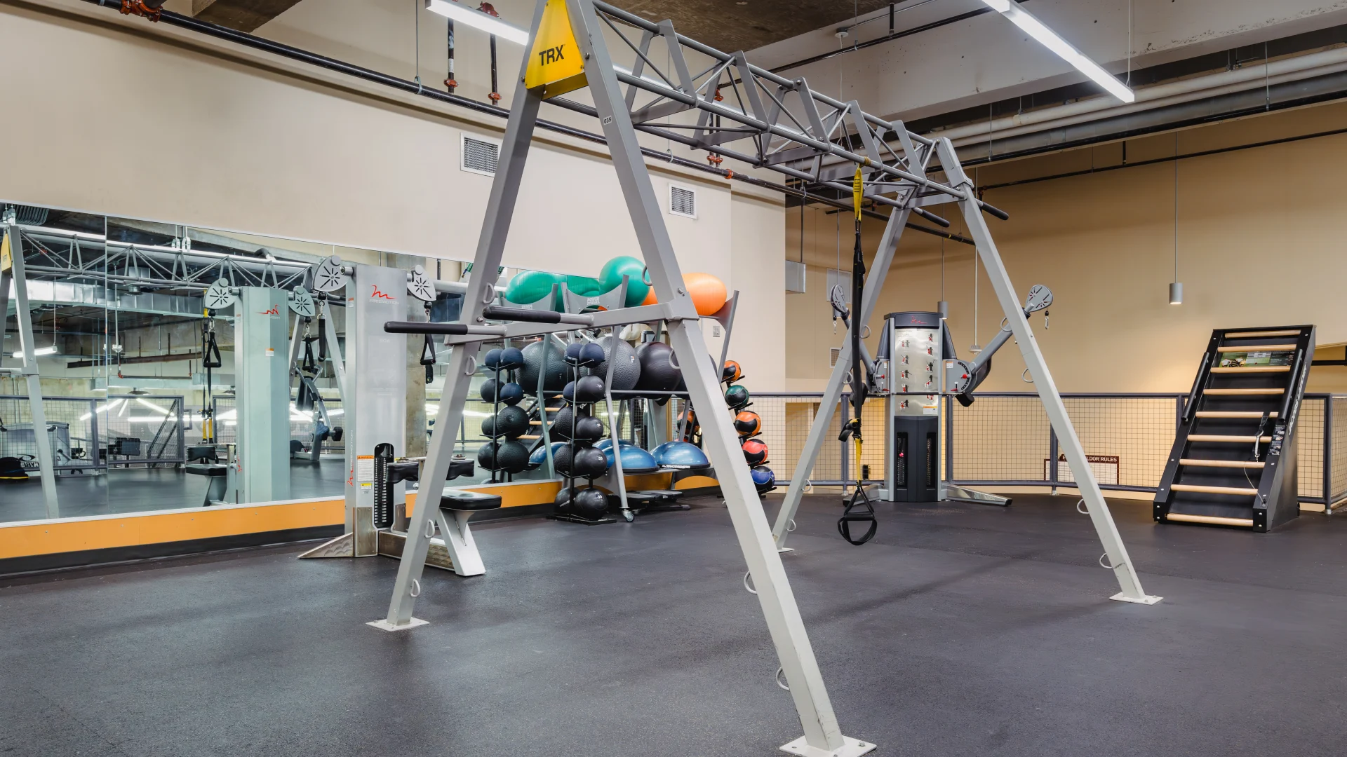 Functional training area at Gold's Gym Austin (Downtown) featuring a TRX training frame, a rack of medicine balls, resistance bands, cable machines, and a stair climber, with large mirrors reflecting the space.