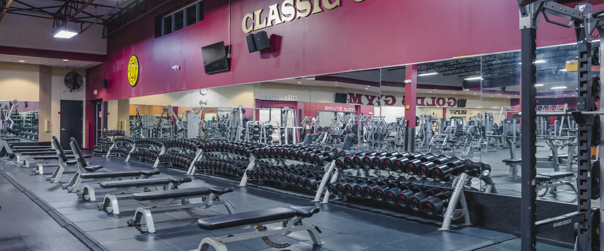 Gold's Gym dumbbell area with mirrored walls, Gold's Gym logo, and a "Classic Gold's" text display.