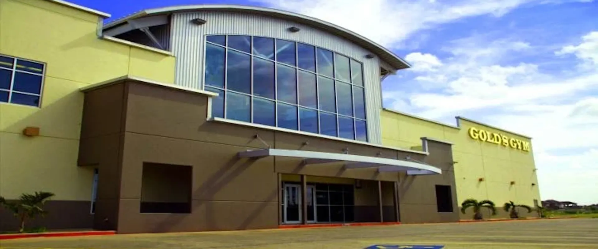 Exterior of Gold’s Gym Laredo Del Mar with large glass windows and yellow signage on a sunny day.
