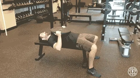 The image shows a person lying on the floor of what appears to be a gym or fitness center, with various exercise equipment and storage racks visible in the background.