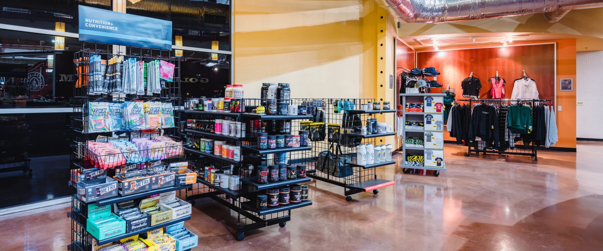 A well-stocked Gold’s Gym Pro Shop showcasing branded apparel, including t-shirts, tank tops, gym shorts, and bags neatly displayed on racks and shelves.