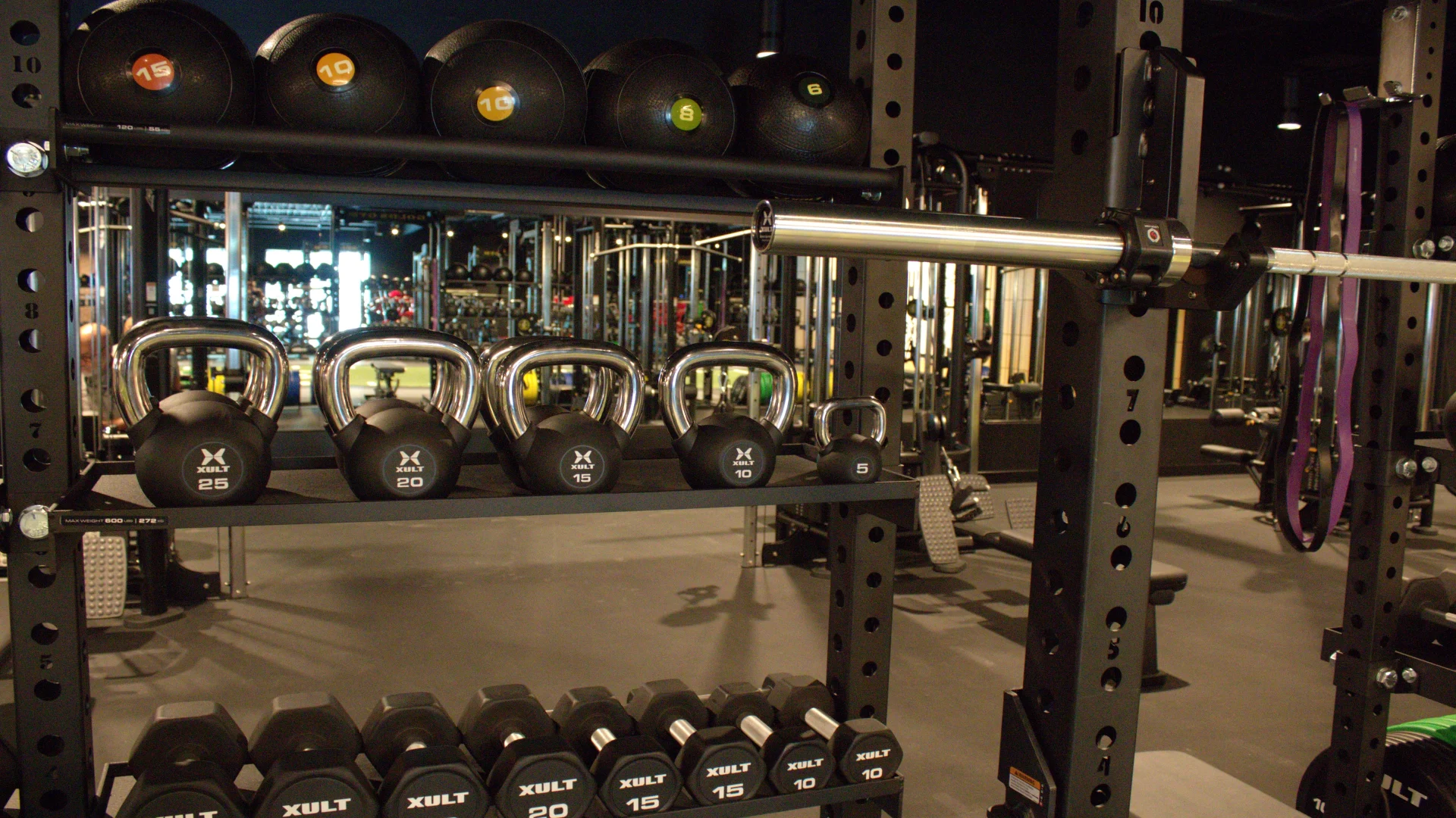 Functional training area at Gold's Gym Austin, Burnet Rd with a neatly organized rack of kettlebells, dumbbells, medicine balls, and resistance bands, all set against mirrored walls and strength equipment.