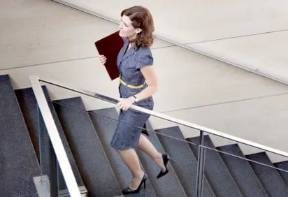 A woman in a denim outfit stands on a staircase with a red wall in the background.