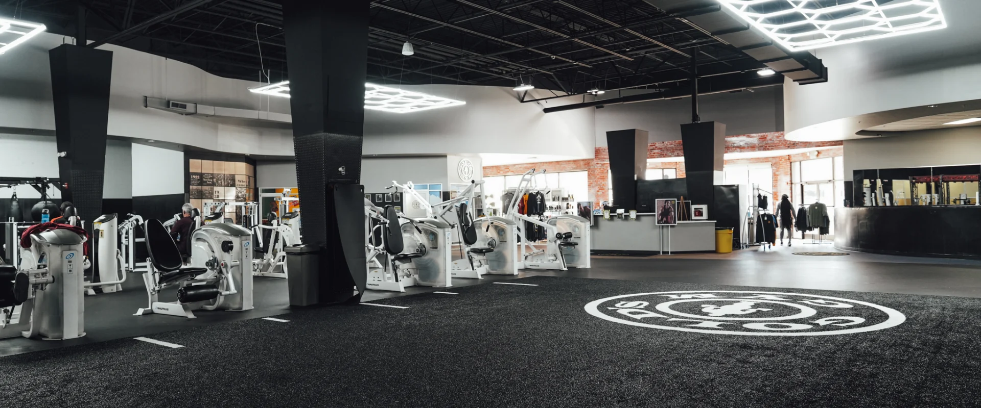 A wide view of the strength training floor at Gold’s Gym Randleman showing resistance machines, a central turf area with the Gold’s Gym logo, and LED lighting panels overhead.