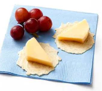 The image shows a plate with two slices of cheese on crackers, accompanied by a cluster of red grapes on a blue and white striped cloth.