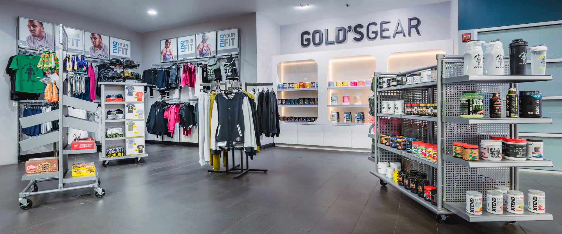 Pro Shop area at Gold's Gym Oklahoma City (Moore), featuring racks of branded apparel, fitness gear, supplements, and protein products, with "Gold's Gear" signage and well-lit display shelves.