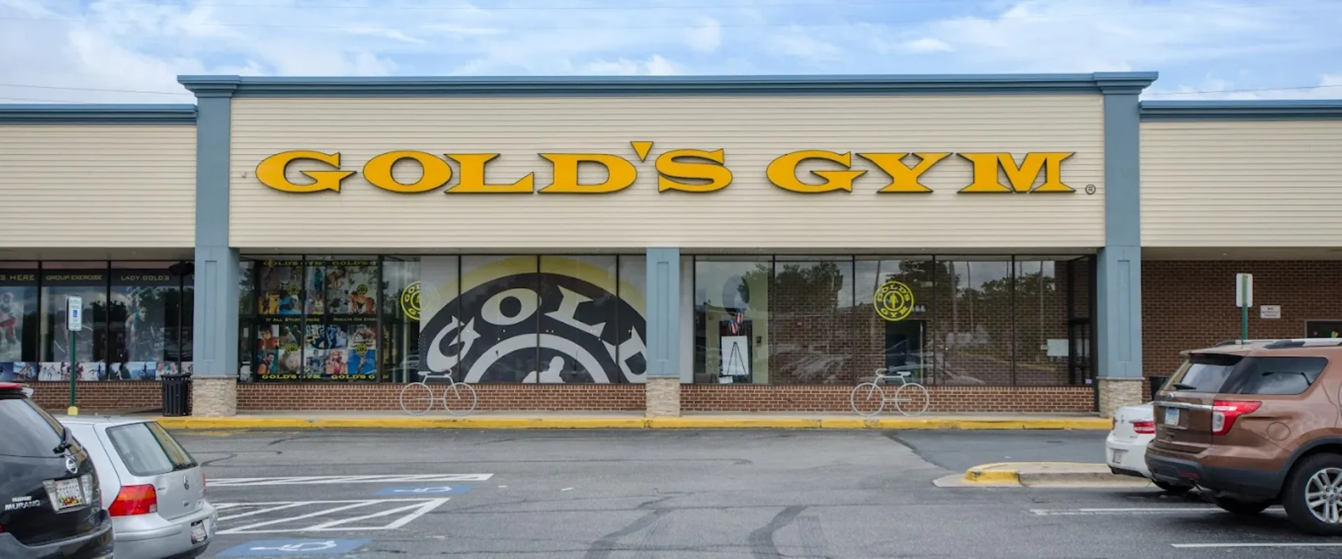 Exterior of Gold’s Gym Dundalk with large yellow signage, window graphics, and front parking area.