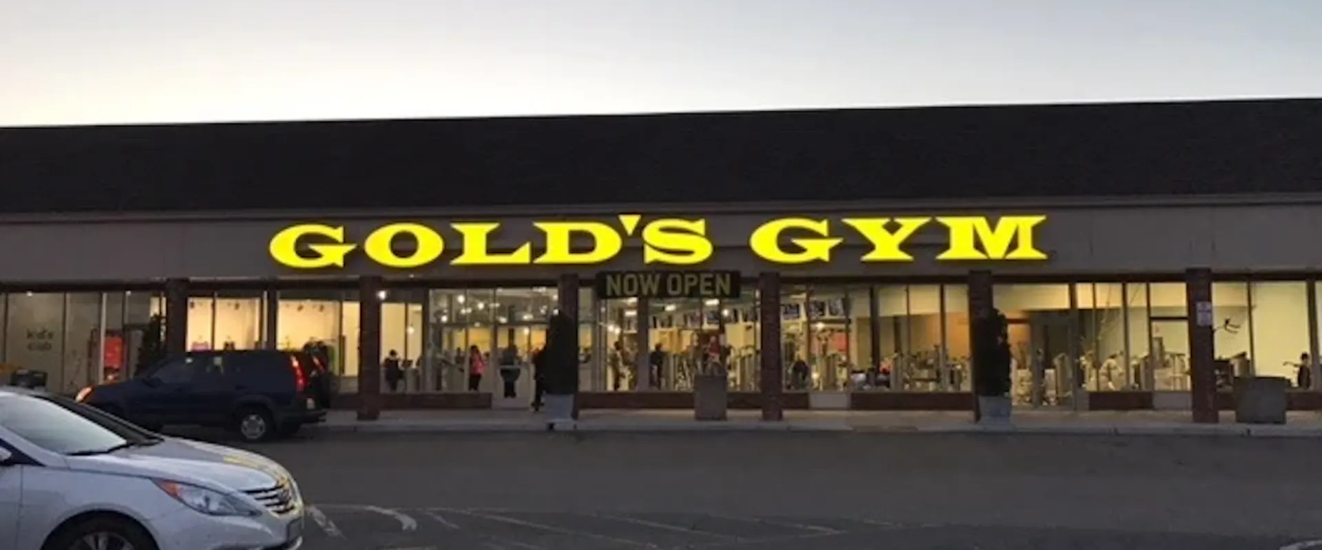 Exterior of Gold’s Gym Meadowbrook with yellow illuminated sign and large glass windows in a shopping plaza.
