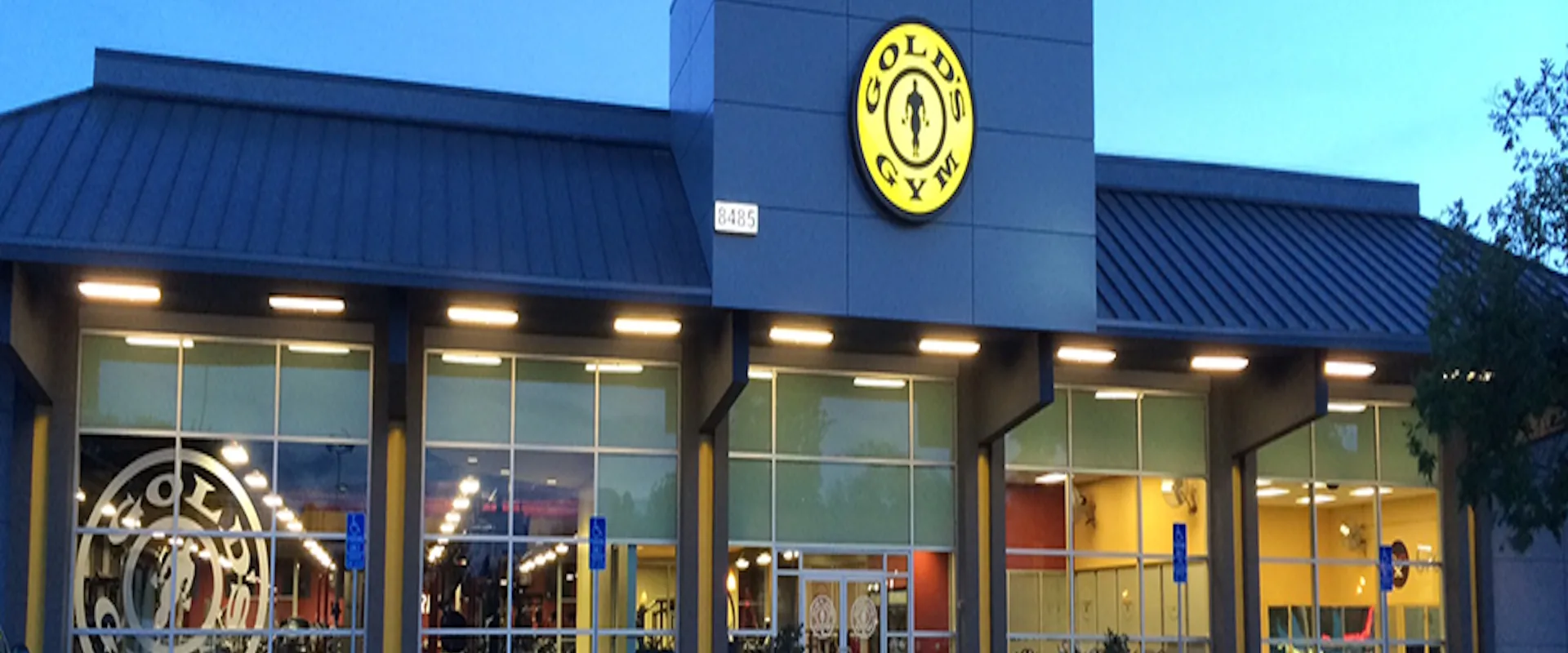 Exterior of Gold’s Gym Citrus Heights with bright yellow logo and glass windows illuminated at dusk.