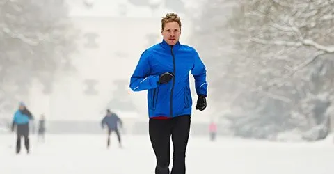 A person in a bright blue jacket stands in a snowy, blurred background with other figures visible in the distance.