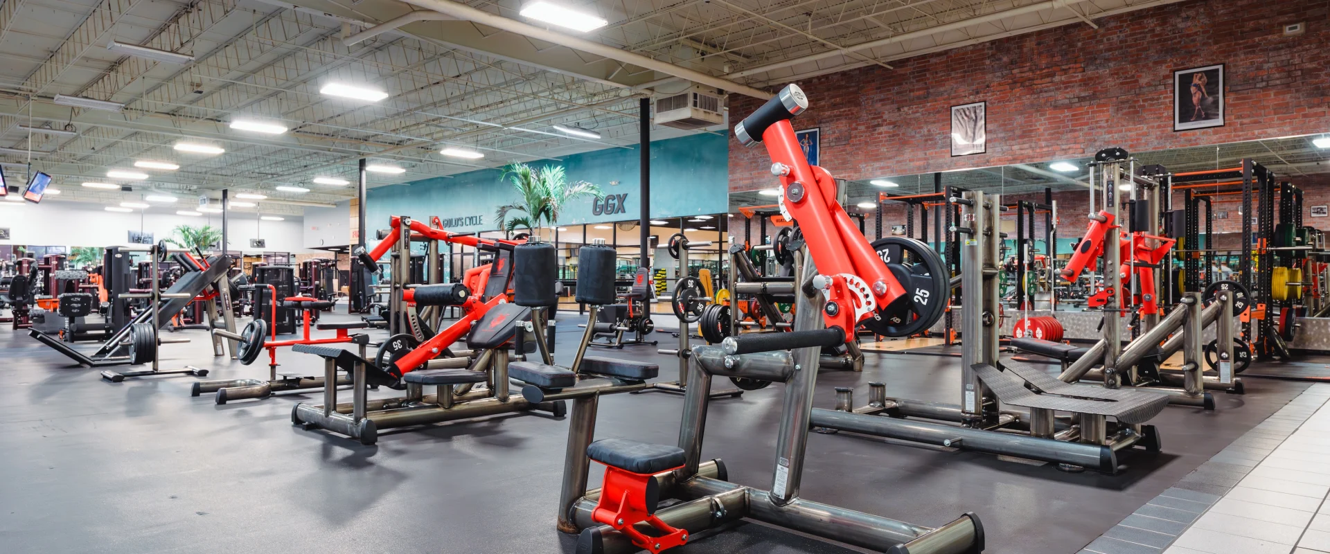 Various red and black exercise machines on a black floor, with high ceilings and bright overhead lighting, conveying an energetic and inviting atmosphere.