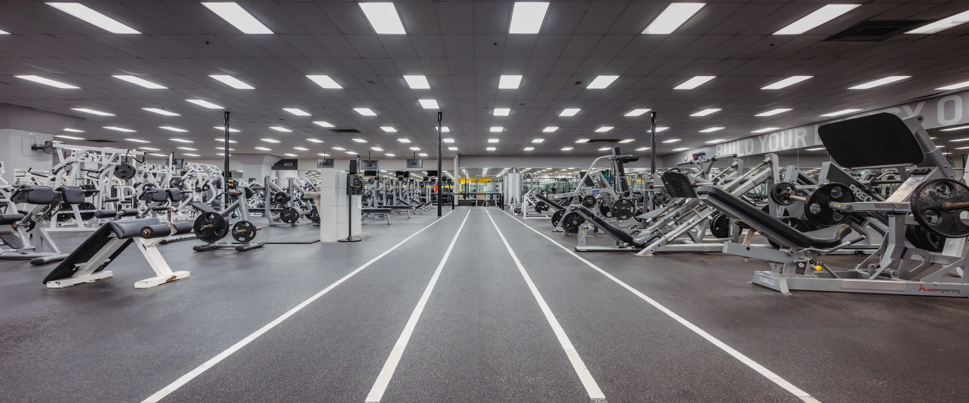 Running track at Gold’s Gym in Austin (South Central), featuring a straight, multi-lane track with white lane markings on rubber flooring. The track runs through the strength training area, flanked by plate-loaded machines, free weights, and resistance equipment. Overhead lighting and mirrored walls create an open, bright environment for both cardio and strength workouts.