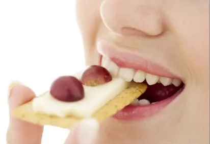 The image shows a close-up of a person's mouth biting into a piece of yellow cake or bread, with red berries or cherries visible.