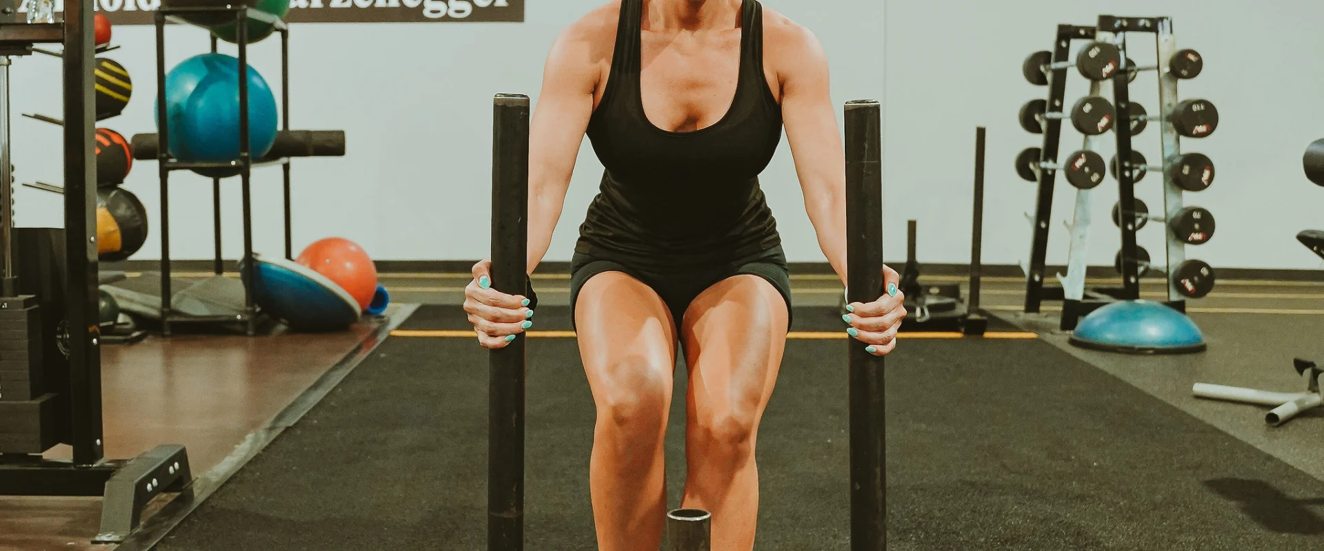 Woman performing a sled push in the functional training area at Gold's Gym Smyrna, Tennessee, with weighted plates loaded on the sled and exercise equipment visible in the background.