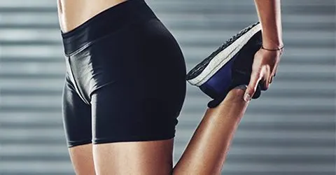 The image shows a person's lower body wearing black athletic shorts and shoes, standing in front of a blurred background.