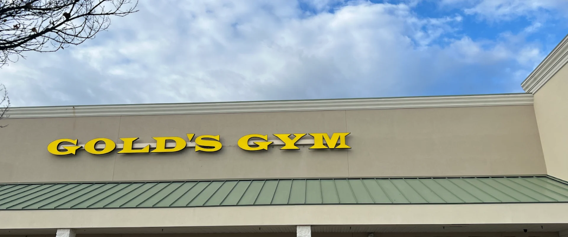 Exterior of Gold’s Gym New Bern with tan walls, green roof, and yellow signage above the entrance doors.