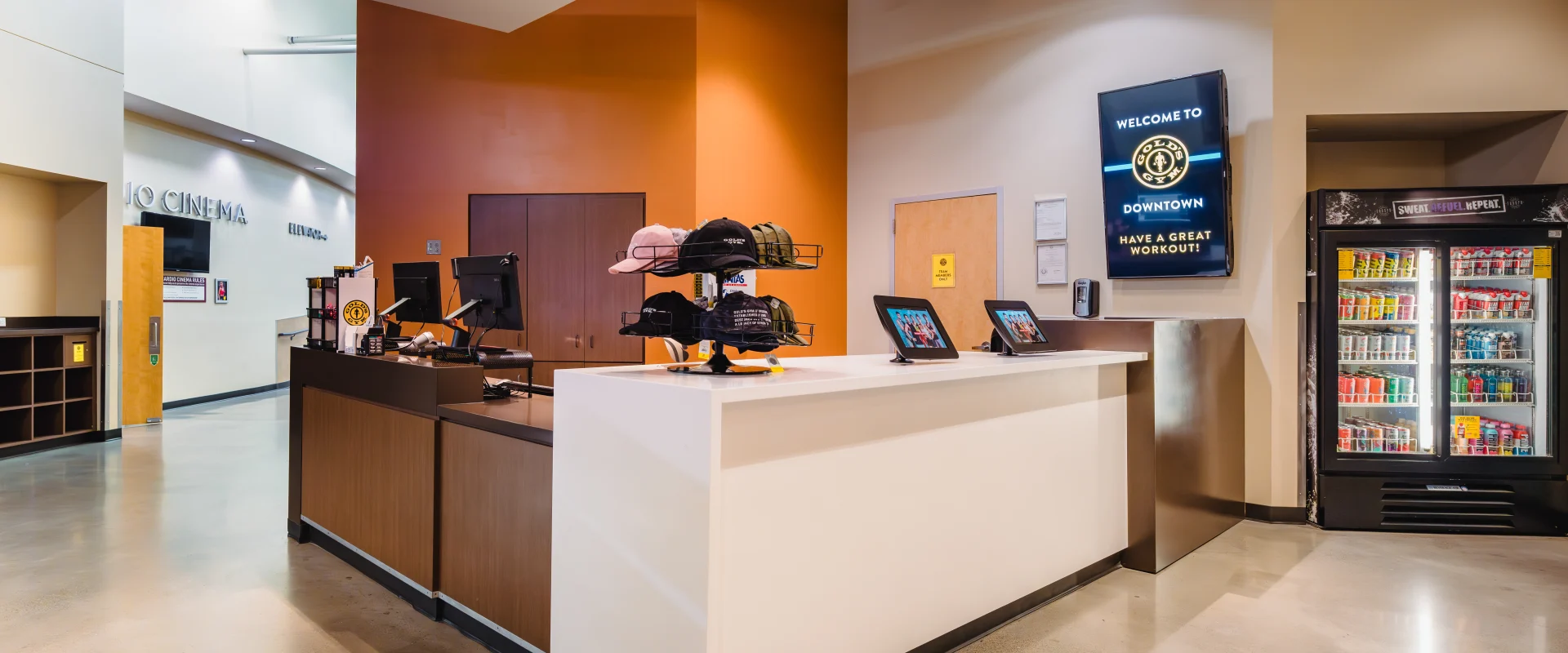 Front desk area at Gold's Gym Austin (Downtown) featuring a reception counter, merchandise display, digital tablets, a drink cooler, and a TV displaying a welcoming message for guests.