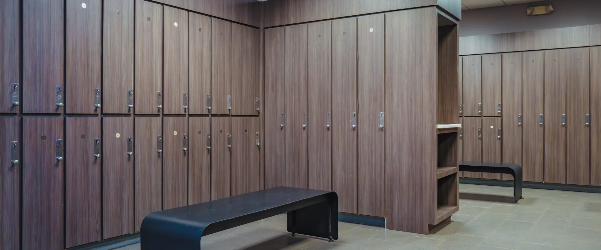 Locker room at Gold's Gym Oklahoma City (Moore), featuring wood-paneled lockers with built-in locks, modern black seating, and tiled flooring under bright overhead lighting.