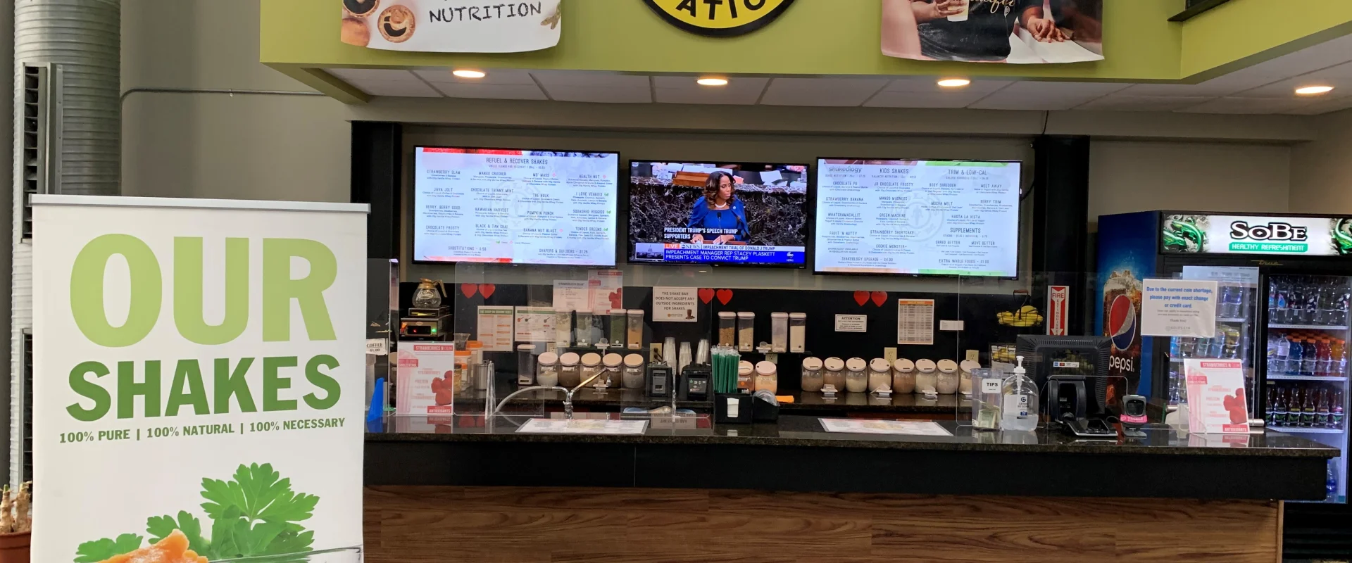 The image shows the interior of a Fuel Station, with a counter displaying various products and signage promoting their shakes. The background includes television screens displaying information, and the walls are decorated with posters and branding elements.