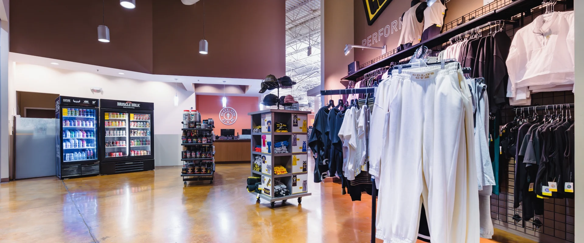 Brightly lit Pro Shopwith wooden flooring, clothing racks displaying activewear, and a refrigerated section with drinks. Modern, inviting atmosphere.
