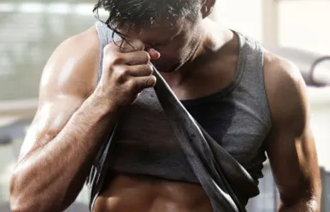 A muscular man in a black tank top is shown in the foreground, with a focused expression as he grips a resistance band in his hands.