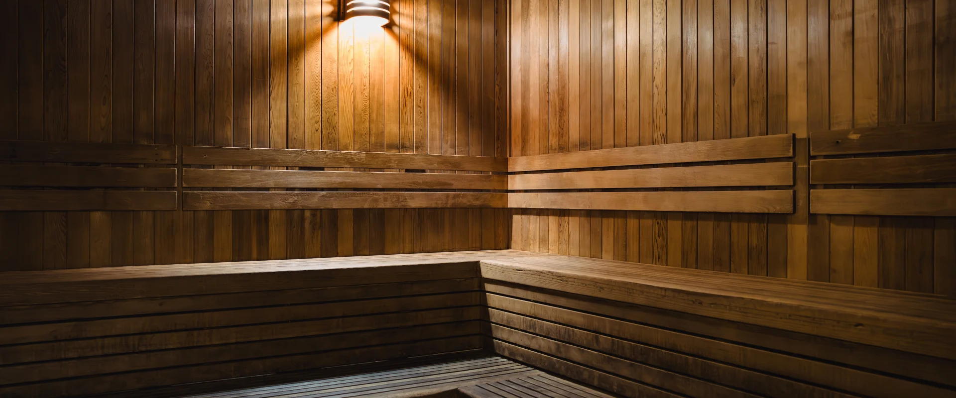 Sauna at Gold's Gym in Texas (Pflugerville), featuring warm wooden paneling and tiered bench seating. A soft, ambient light fixture casts a gentle glow, enhancing the cozy, relaxing atmosphere designed for post-workout recovery.