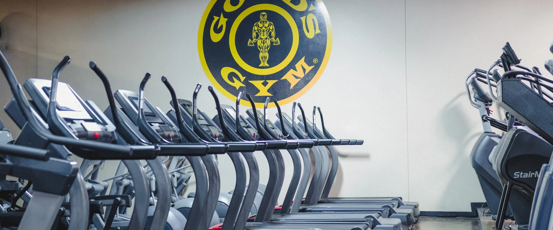 Row of treadmills in a Gold's Gym fitness center with branded logo visible on wall.