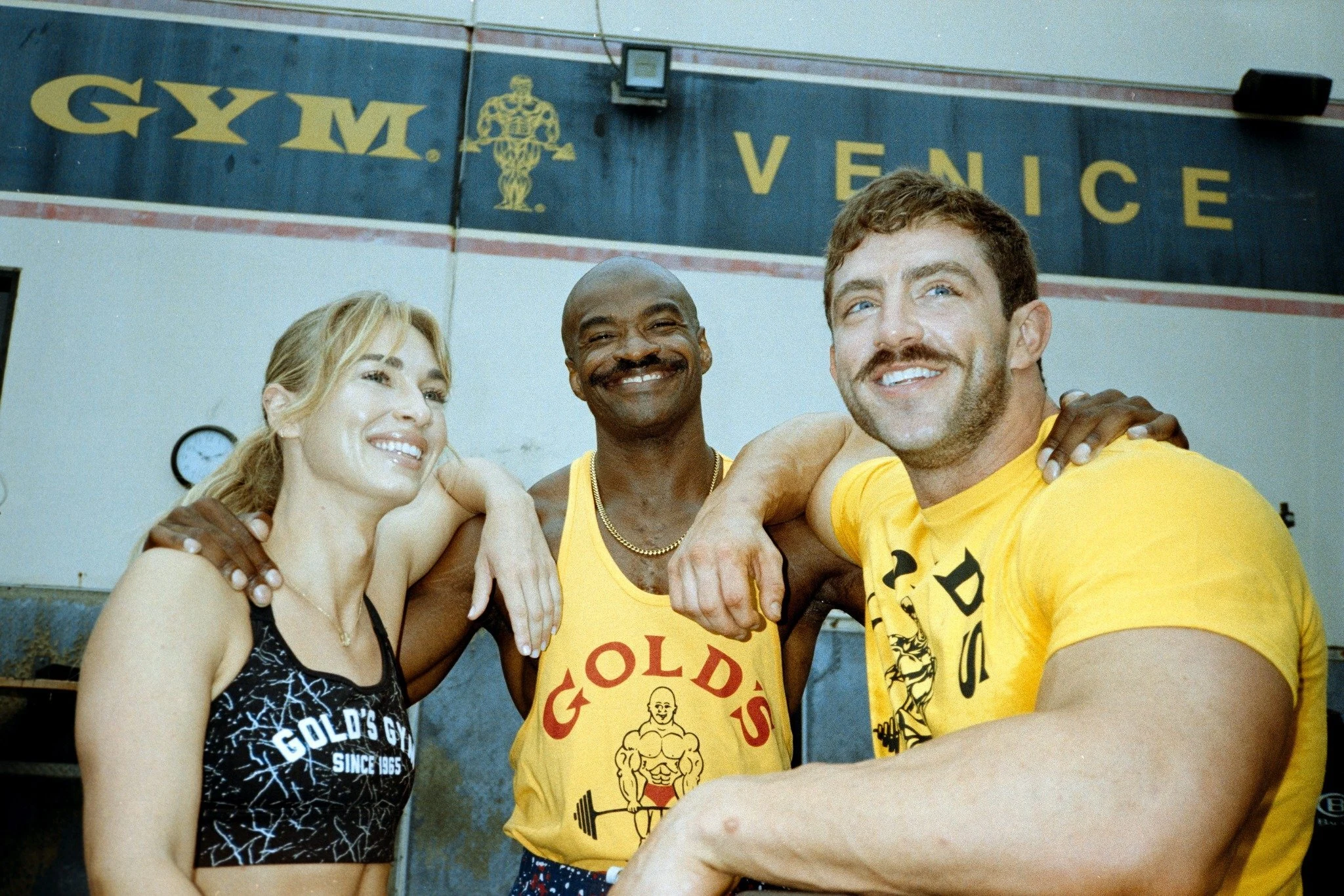 Gold's Gym members smiling and flexing in front of iconic gym backdrop