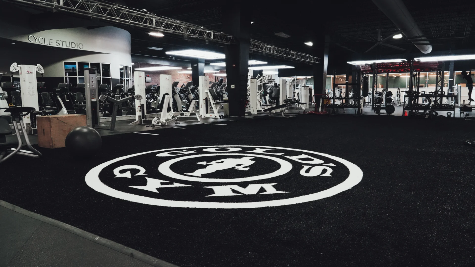 A functional training zone at Gold's Gym Brassfield, featuring a black turf area with the Gold’s Gym logo in the center. The space is surrounded by cable machines, squat racks, and cardio equipment. A wooden plyometric box and medicine ball rest on the turf, ready for performance training.