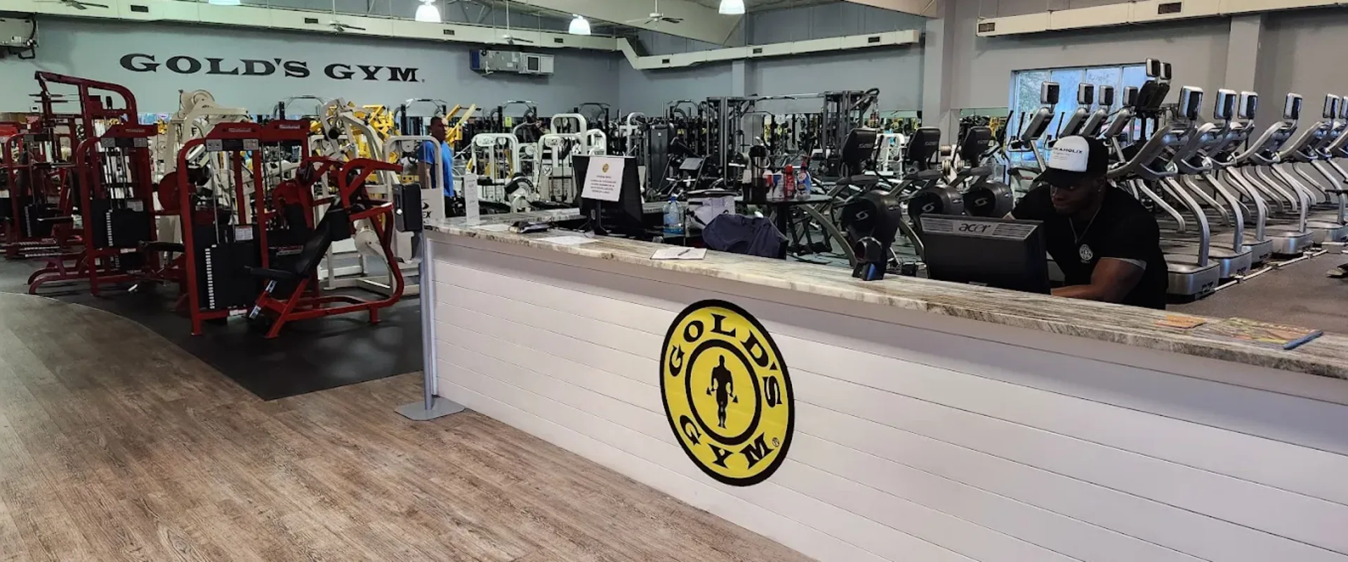 Interior of Gold’s Gym Destin with front desk, cardio machines, and strength equipment in a bright gym space.