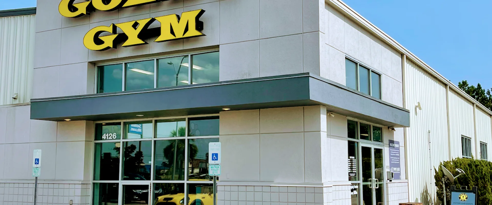 Exterior of Gold’s Gym Jacksonville with yellow signage and glass entrance in a light gray building.