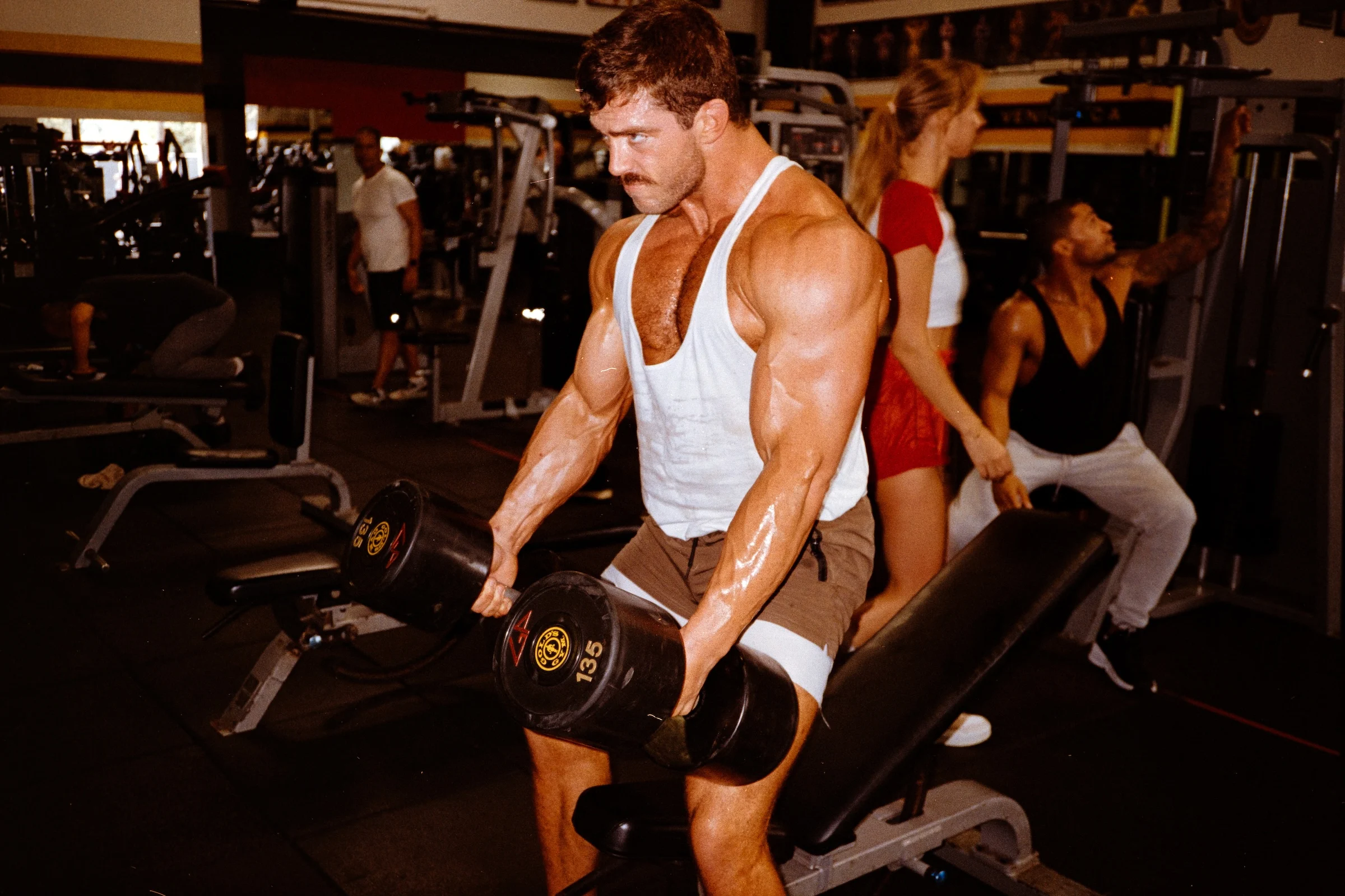 Man performing a heavy dumbbell hold at Gold’s Gym.