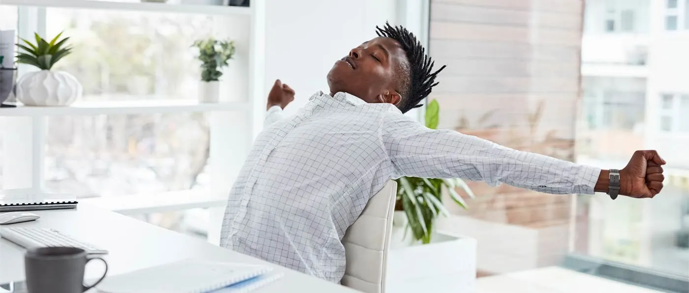 A person with a mohawk hairstyle wearing a white checkered shirt stands in a room with a window in the background.