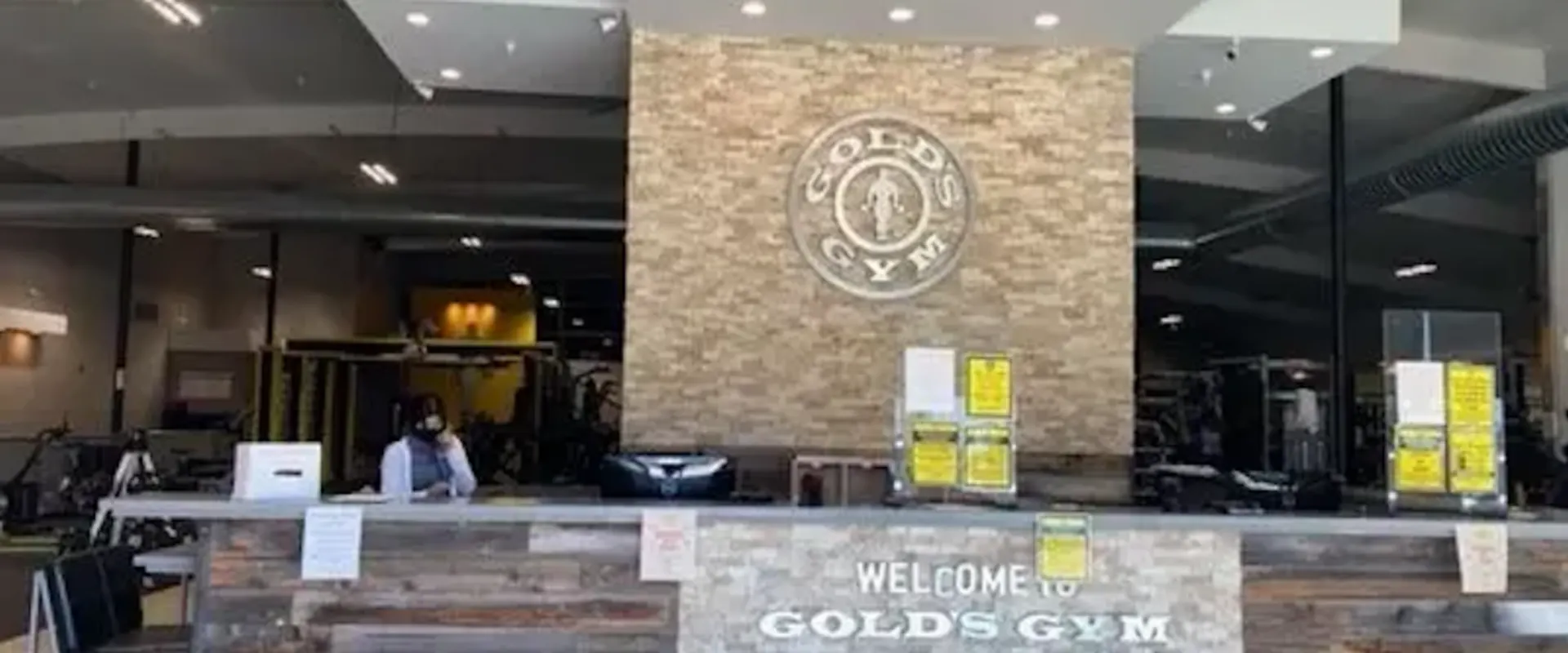 Front desk of Gold’s Gym Hollister with stone accent wall, Gold’s Gym logo, and modern reception area.