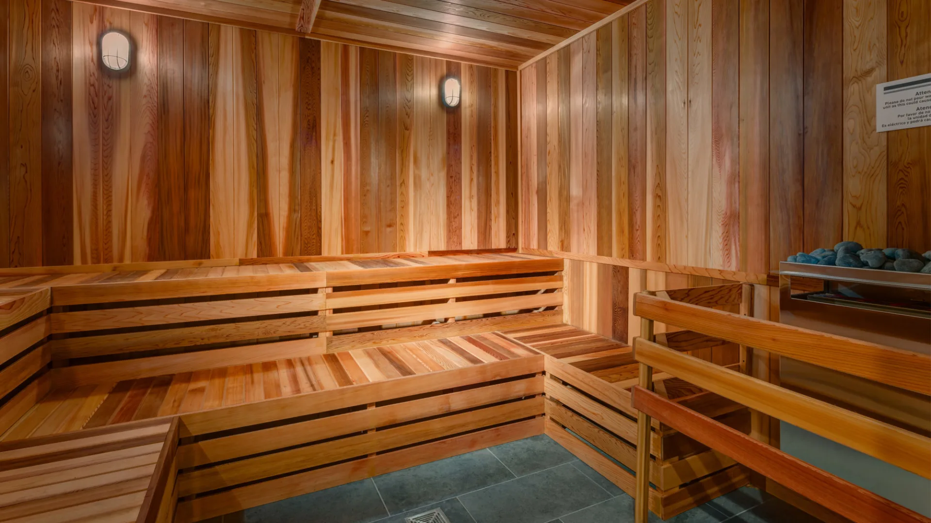 A cozy and warm-toned wooden sauna interior with benches, shelves, and lighting fixtures, creating a serene and relaxing atmosphere.