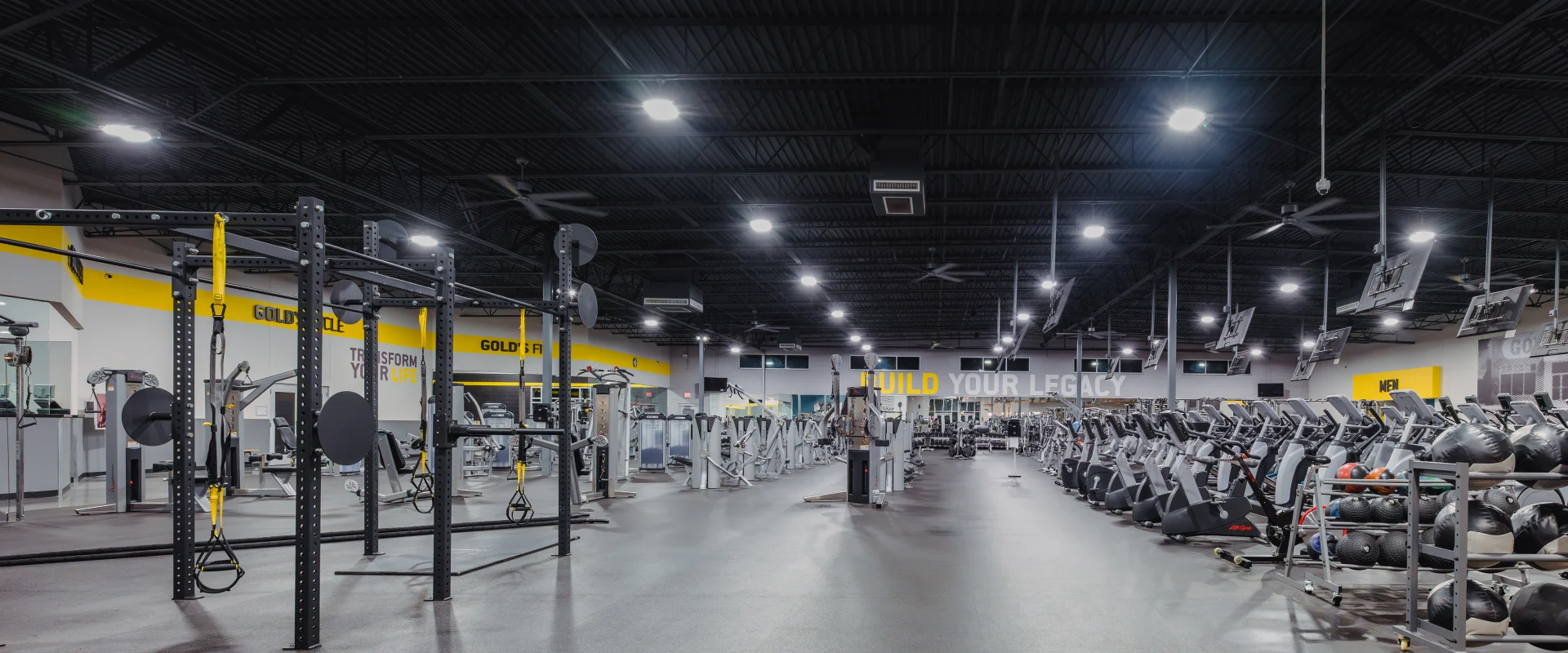 Main gym floor at Gold’s Gym, featuring power racks, rows of treadmills, cardio machines, free weights, and functional training equipment under high industrial ceilings with bright lighting.