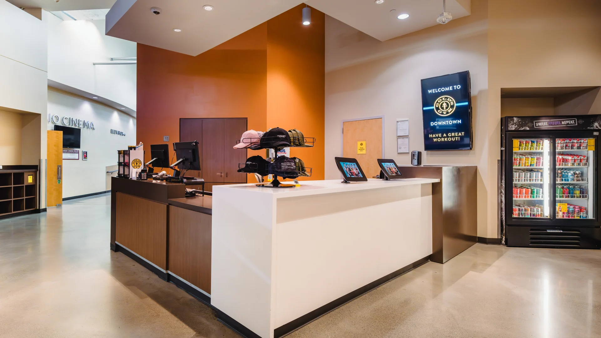 Front desk area at Gold's Gym Austin (Downtown) featuring a reception counter, merchandise display, digital tablets, a drink cooler, and a TV displaying a welcoming message for guests.
