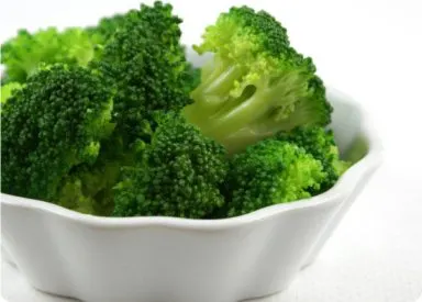 A white bowl filled with fresh, vibrant green broccoli florets, set against a plain white background.